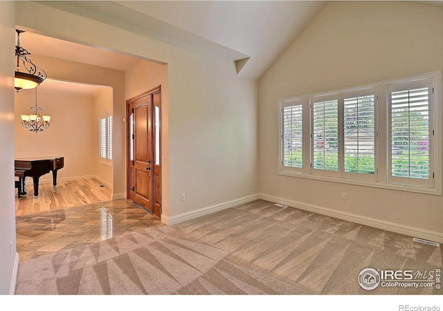 spare room featuring baseboards, carpet floors, a chandelier, wood finished floors, and high vaulted ceiling