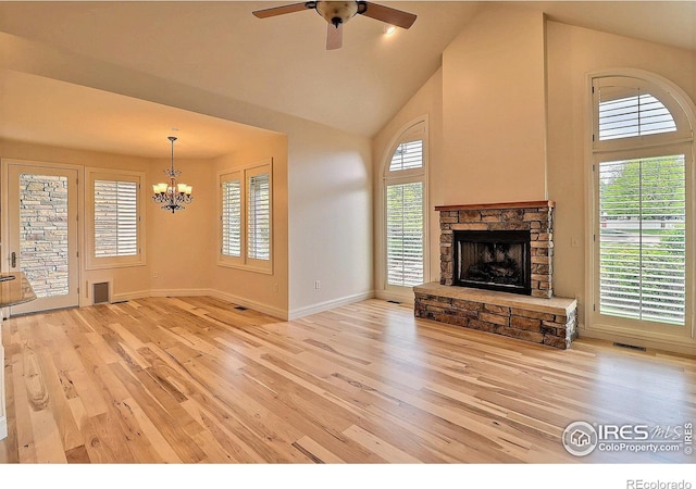 unfurnished living room with light wood-style floors, a chandelier, high vaulted ceiling, a stone fireplace, and baseboards