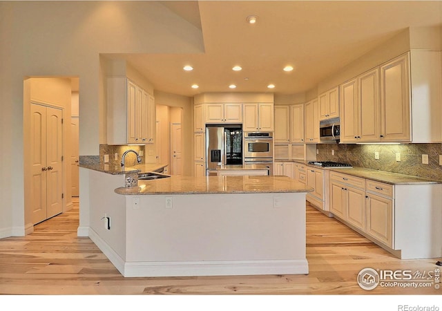 kitchen featuring appliances with stainless steel finishes, a sink, light wood-style flooring, light stone counters, and recessed lighting