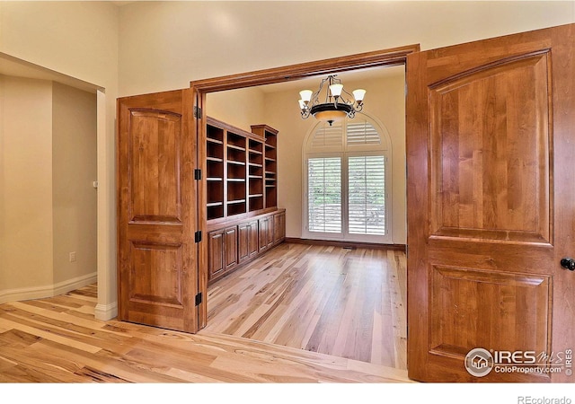 empty room with light wood-style flooring, a chandelier, and baseboards