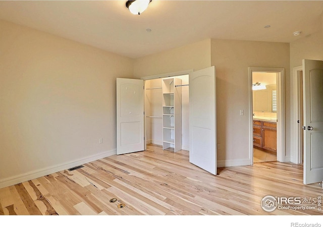 unfurnished bedroom featuring light wood-style floors, a closet, baseboards, ensuite bathroom, and a spacious closet