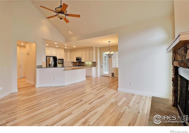 unfurnished living room featuring a chandelier, light wood-style floors, ceiling fan, a stone fireplace, and high vaulted ceiling