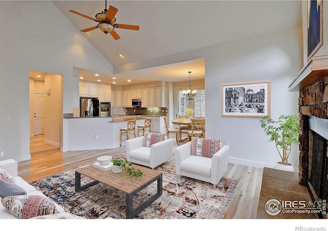 living area featuring a chandelier, light wood-style flooring, ceiling fan, a fireplace with raised hearth, and high vaulted ceiling