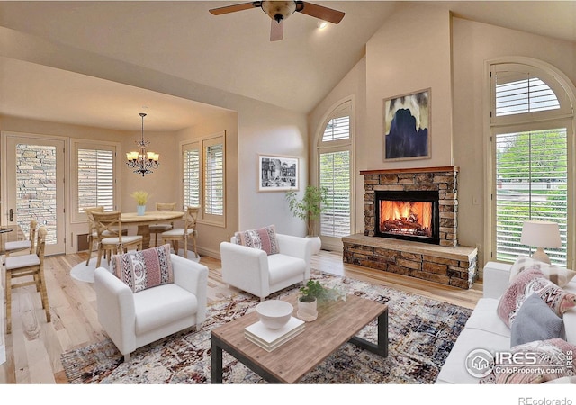living area with high vaulted ceiling, light wood-style flooring, a fireplace, ceiling fan, and a chandelier