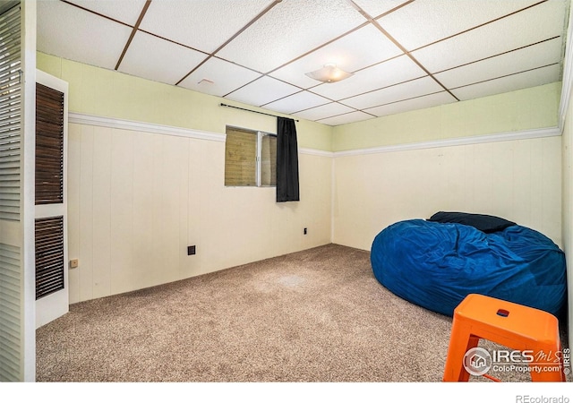 unfurnished room featuring carpet floors, a drop ceiling, and wood walls