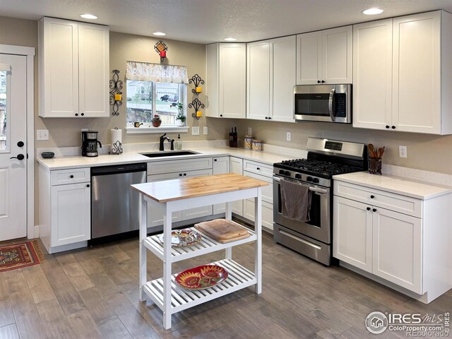 kitchen with stainless steel appliances, a sink, recessed lighting, dark wood finished floors, and white cabinets