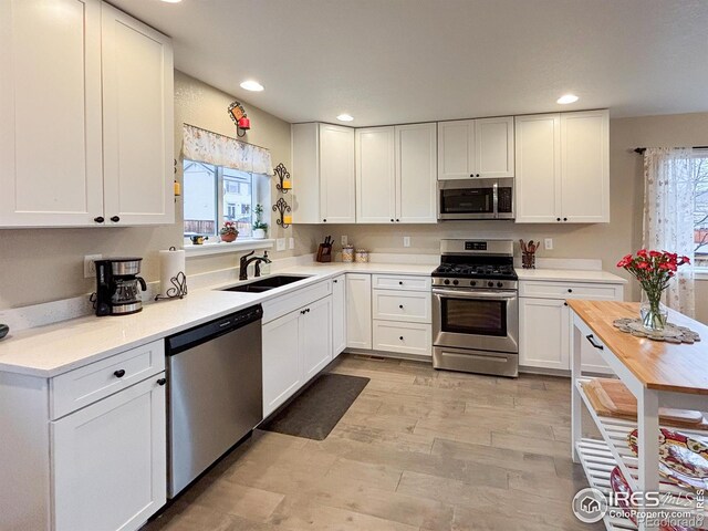 kitchen featuring stainless steel appliances, a sink, white cabinets, light countertops, and recessed lighting
