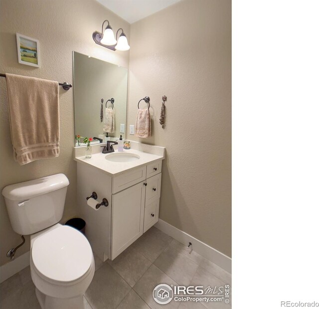 half bath featuring toilet, vanity, tile patterned floors, and baseboards