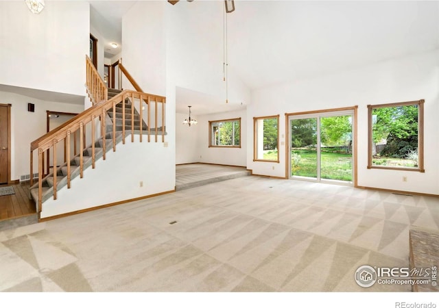 unfurnished living room with high vaulted ceiling, carpet flooring, stairway, baseboards, and a chandelier