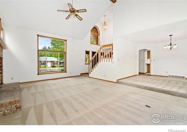 unfurnished living room with carpet flooring, high vaulted ceiling, ceiling fan, stairs, and a chandelier