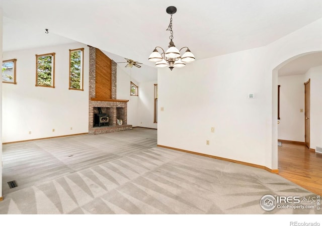 unfurnished living room with arched walkways, baseboards, light colored carpet, a chandelier, and a fireplace
