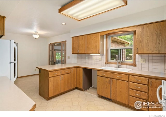 kitchen with freestanding refrigerator, a sink, a peninsula, light countertops, and decorative backsplash