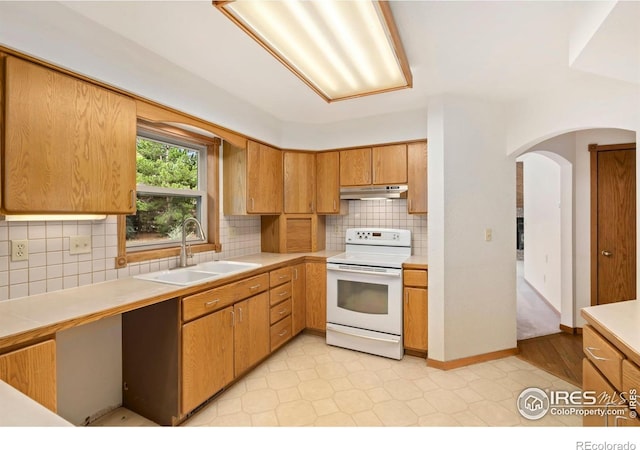 kitchen with white range with electric stovetop, a sink, under cabinet range hood, light countertops, and arched walkways