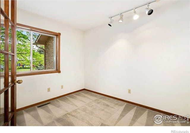 unfurnished room with track lighting, light colored carpet, and baseboards