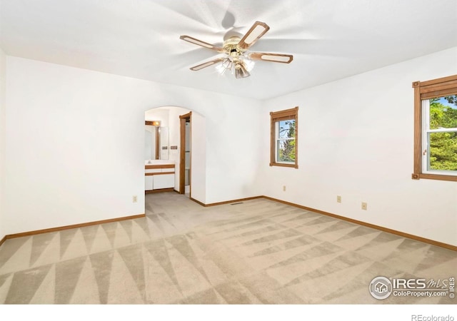 spare room featuring light carpet, arched walkways, baseboards, and ceiling fan