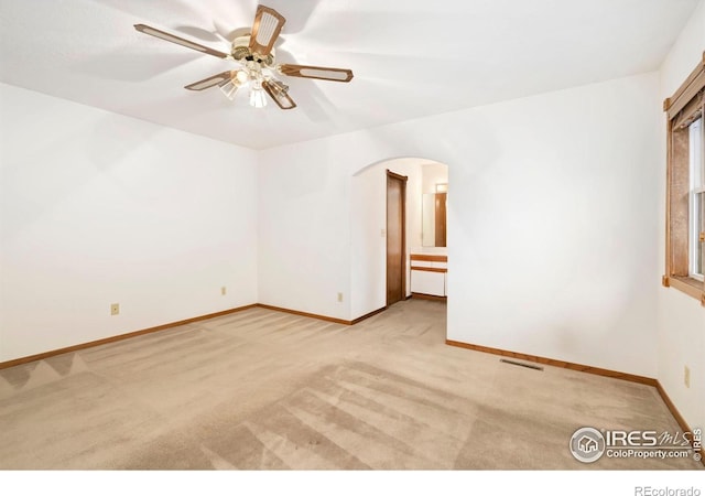 carpeted spare room with arched walkways, ceiling fan, and baseboards