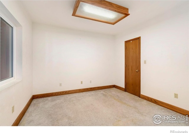 carpeted empty room featuring attic access and baseboards