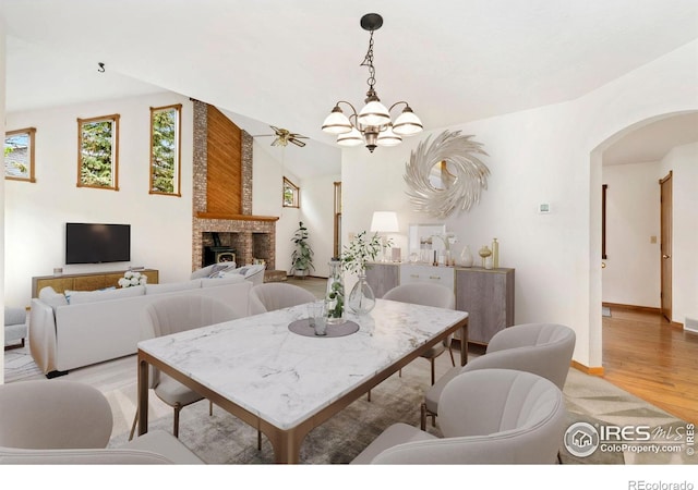 dining space featuring arched walkways, light wood-type flooring, a brick fireplace, a chandelier, and baseboards