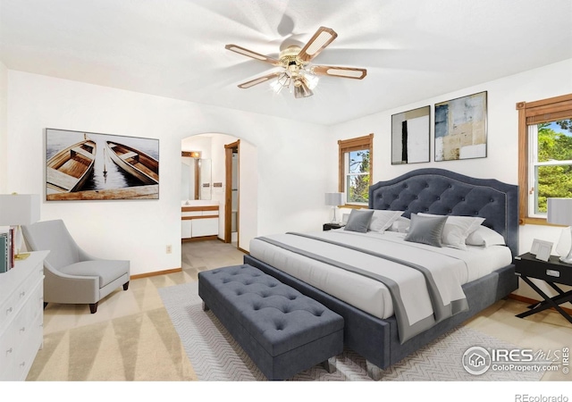 bedroom featuring arched walkways, light carpet, ensuite bathroom, and ceiling fan