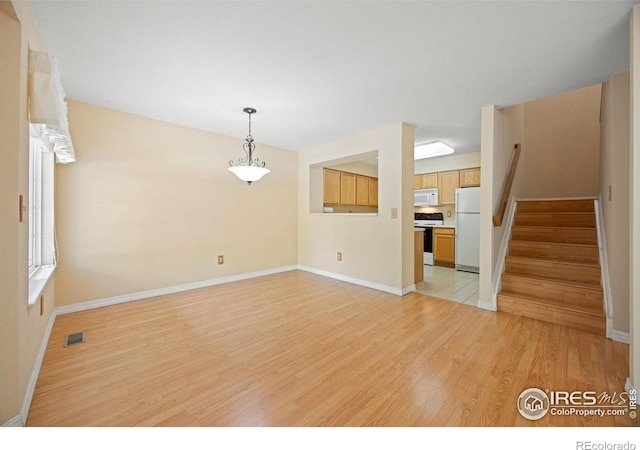 unfurnished living room featuring light wood-style flooring, stairs, and baseboards