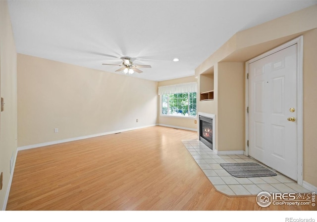 unfurnished living room featuring light wood-type flooring, a ceiling fan, a fireplace with flush hearth, and baseboards
