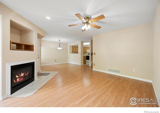 unfurnished living room with light wood-style floors, a tiled fireplace, a ceiling fan, and baseboards