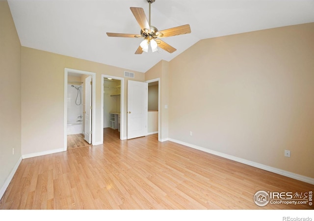 unfurnished bedroom with light wood-style floors, vaulted ceiling, a spacious closet, and baseboards