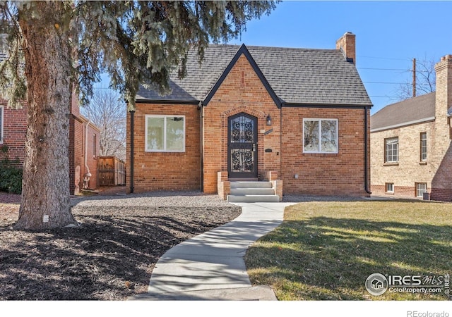 tudor house featuring brick siding, a front yard, and a chimney
