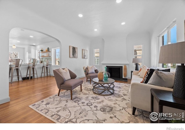 living area featuring arched walkways, recessed lighting, wood finished floors, healthy amount of natural light, and a fireplace