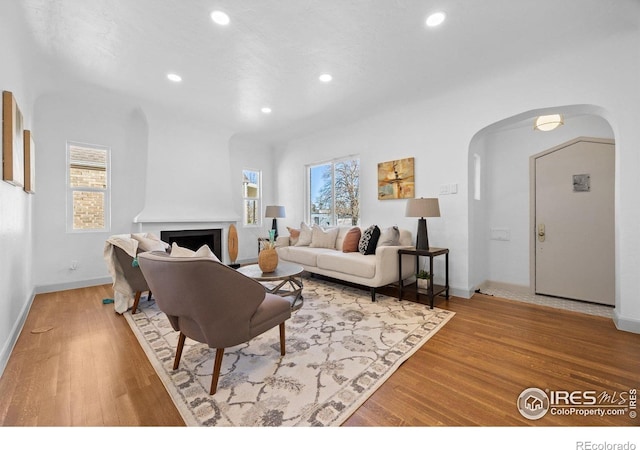 living area featuring arched walkways, recessed lighting, healthy amount of natural light, wood finished floors, and a fireplace