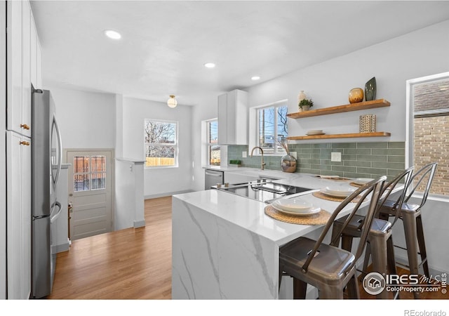 kitchen featuring light stone counters, a sink, white cabinetry, tasteful backsplash, and light wood-type flooring