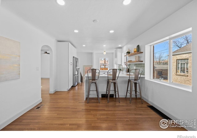 kitchen with freestanding refrigerator, a kitchen breakfast bar, white cabinets, wood finished floors, and a peninsula