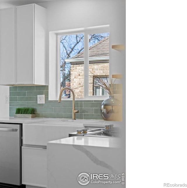 kitchen featuring stainless steel dishwasher, white cabinets, light countertops, and backsplash