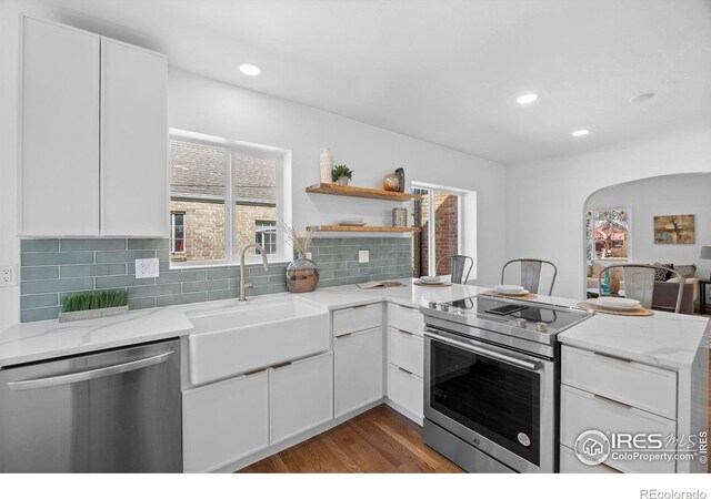 kitchen with appliances with stainless steel finishes, a sink, a peninsula, dark wood finished floors, and white cabinets