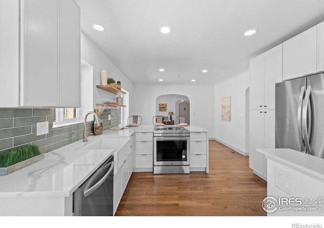 kitchen featuring appliances with stainless steel finishes, open shelves, arched walkways, recessed lighting, and decorative backsplash