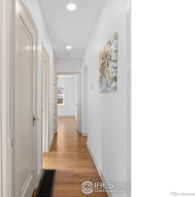 hall featuring arched walkways, wood finished floors, baseboards, and recessed lighting