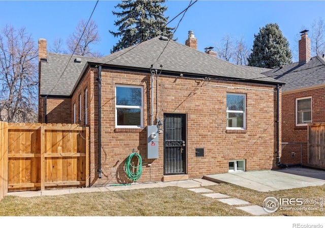 back of property with brick siding, a chimney, a shingled roof, fence, and a patio area