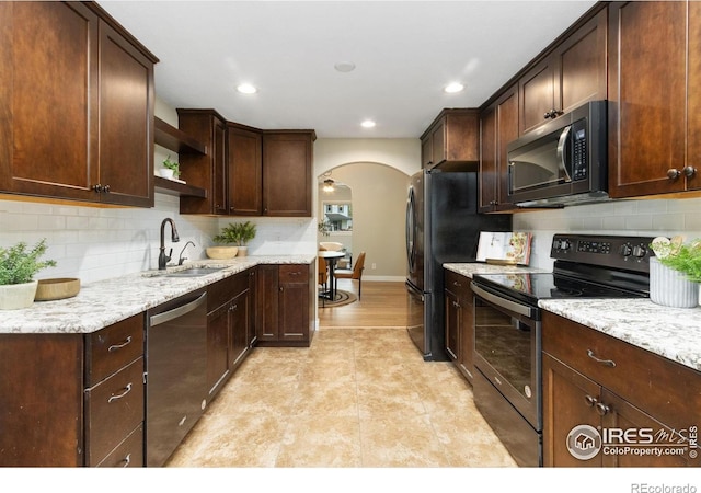 kitchen featuring stainless steel appliances, a sink, arched walkways, open shelves, and backsplash