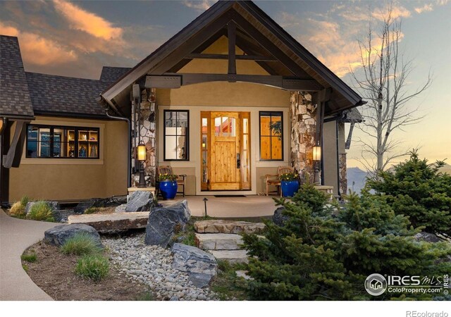 view of front of property with stone siding, stucco siding, covered porch, and roof with shingles