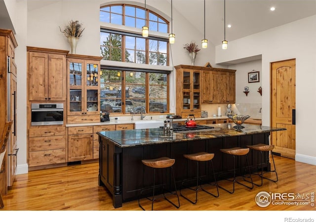 kitchen with high vaulted ceiling, brown cabinets, light wood-style floors, a kitchen bar, and recessed lighting