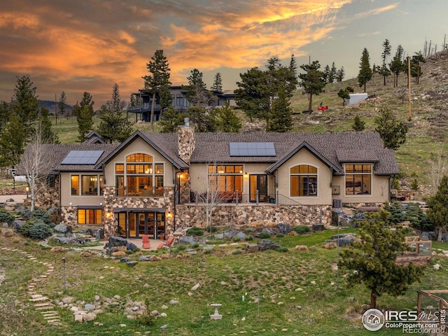 back of property at dusk featuring roof mounted solar panels, a chimney, stucco siding, and a patio area