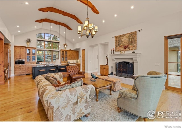 living area with light wood-style flooring, recessed lighting, a fireplace with raised hearth, a chandelier, and high vaulted ceiling
