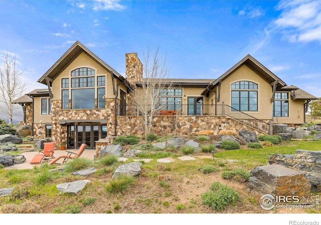 view of front of property featuring stucco siding, a chimney, stone siding, a patio, and stairs