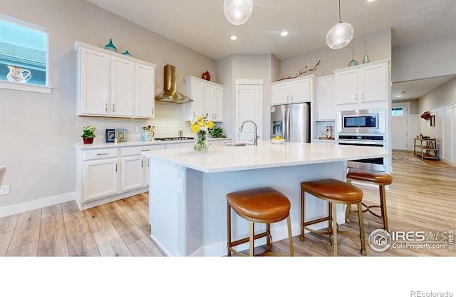 kitchen featuring stainless steel appliances, wall chimney range hood, a sink, white cabinets, and recessed lighting
