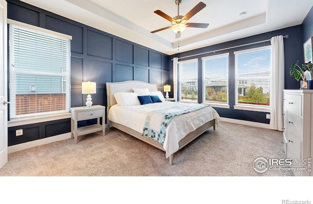bedroom featuring a decorative wall, light colored carpet, a raised ceiling, and ceiling fan