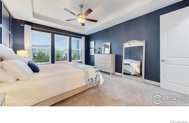 carpeted bedroom featuring a tray ceiling, baseboards, and ceiling fan