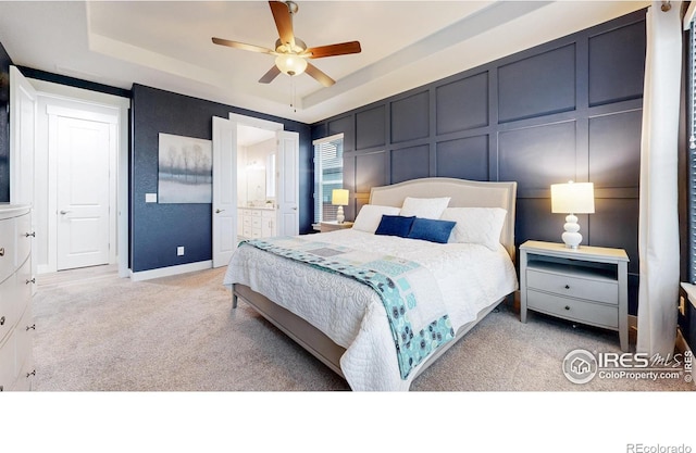 bedroom with carpet floors, a decorative wall, a raised ceiling, baseboards, and connected bathroom