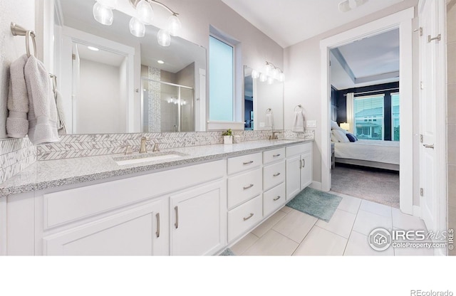 bathroom with a shower stall, tile patterned floors, double vanity, ensuite bathroom, and baseboards
