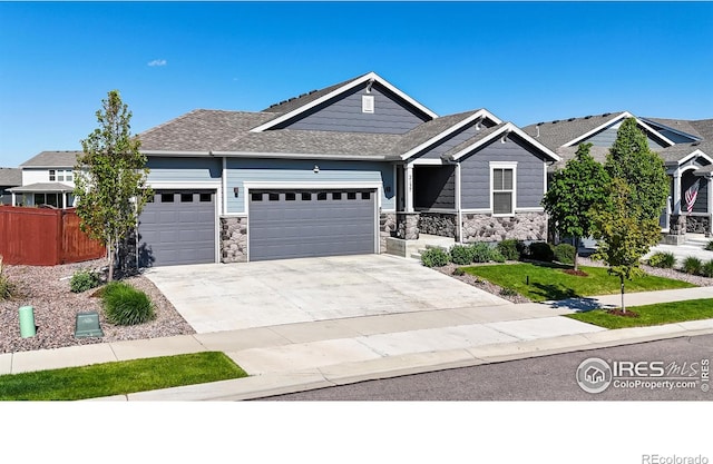 2137 Setting Sun Dr, Windsor, CO 80550 - craftsman-style house featuring a garage, driveway, fence, and stone siding