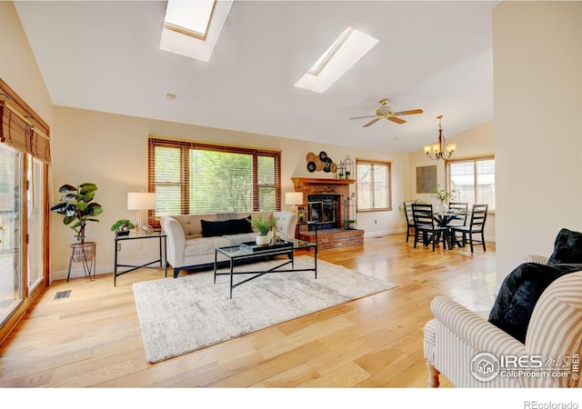 living area with lofted ceiling, a skylight, light wood-style floors, a brick fireplace, and a chandelier